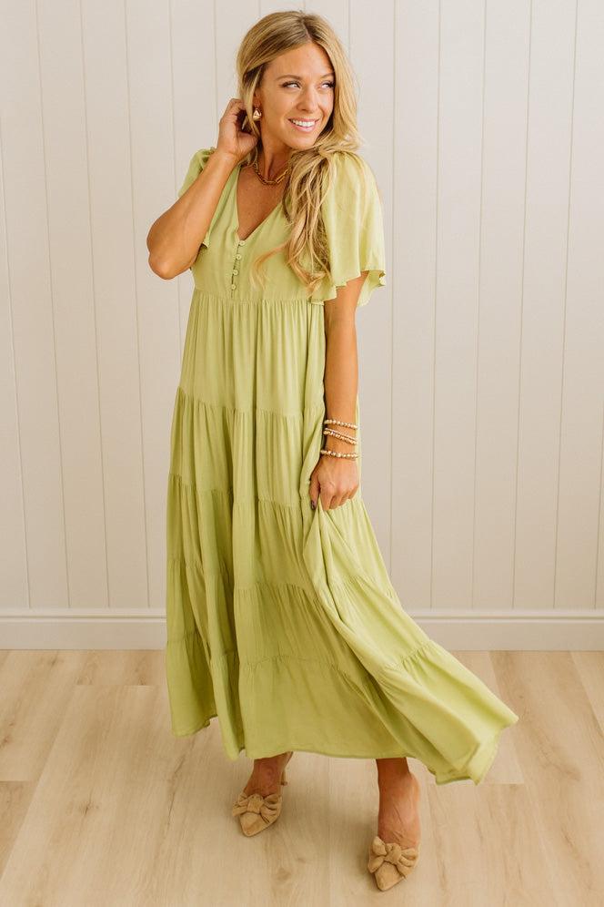 Woman wearing a light green dress standing against a white wall.