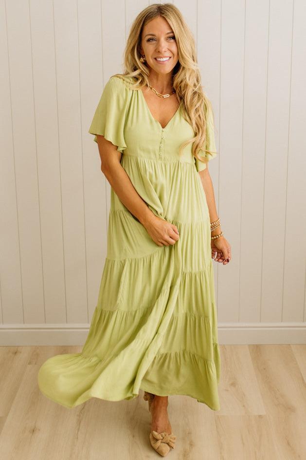 Woman wearing a light green dress standing against a white paneled wall.