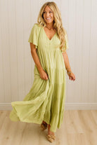 Woman wearing a light green dress standing against a white paneled wall.