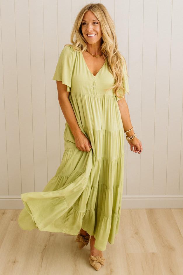 Woman wearing a light green dress standing against a white paneled wall.