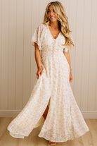 Woman wearing a white floral dress against a beige wall.