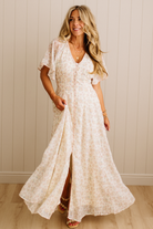 Woman wearing a white lace dress against a beige wall.