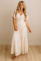 Woman wearing a white floral dress standing against a wooden paneled wall.