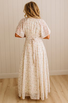 Woman wearing a floral dress standing against a white paneled wall.