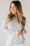 Blonde woman wearing a lightweight sweater with grey and white stripes with light green trim at neckline, wrist and hem.