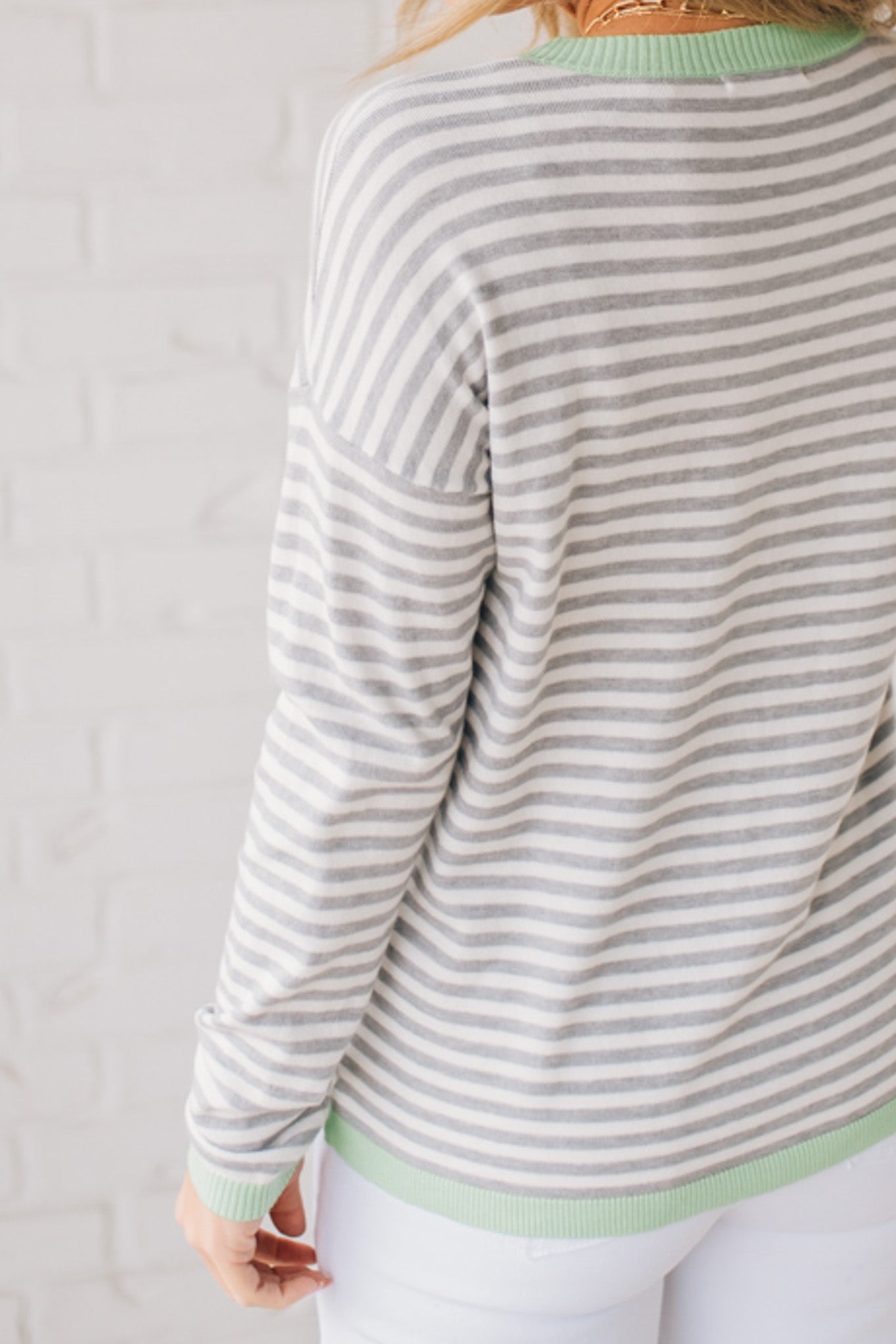 Blonde woman wearing a lightweight sweater with grey and white stripes with light green trim at neckline, wrist and hem.