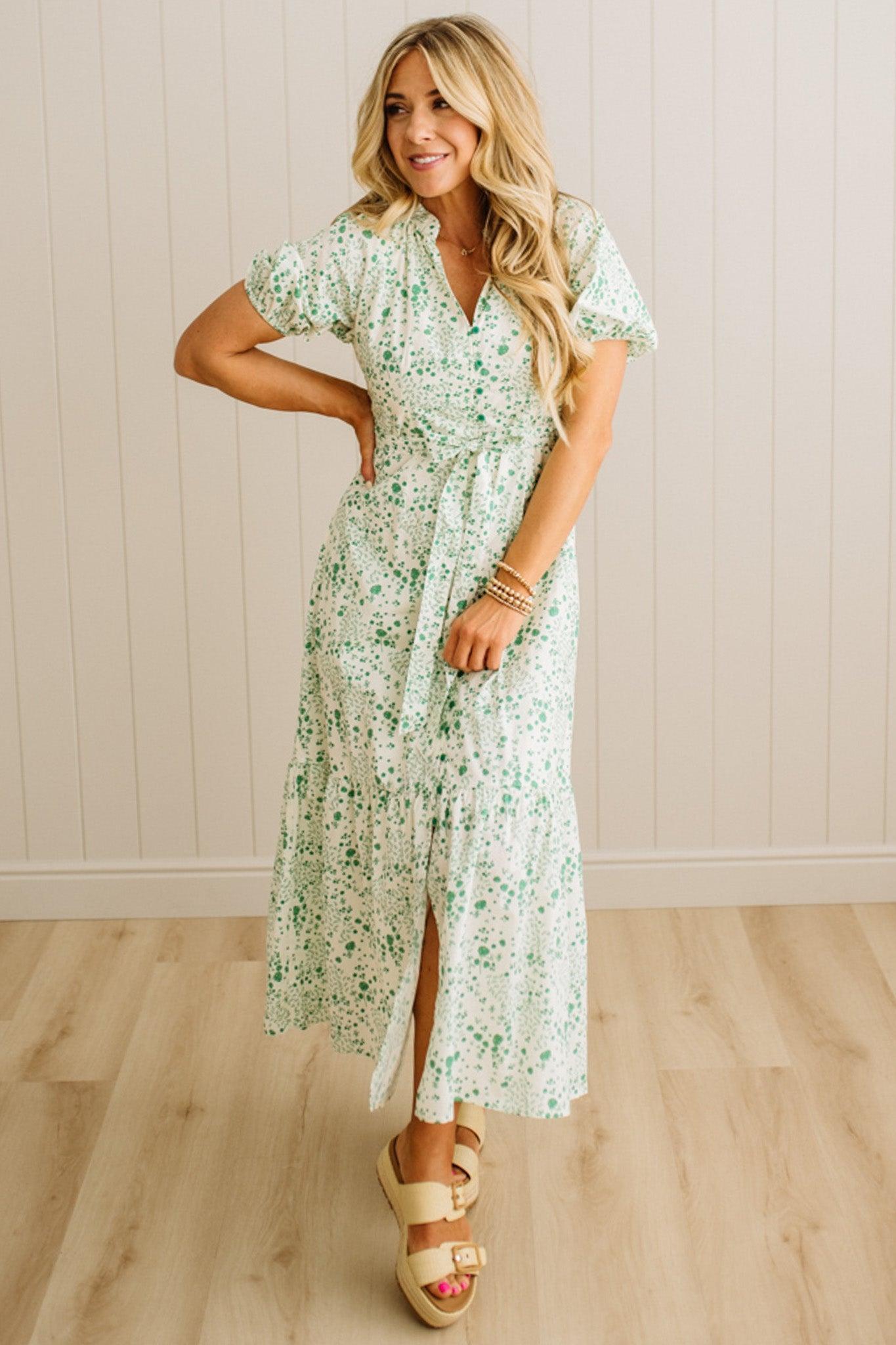 Woman wearing a floral dress standing in a room with wooden flooring and a white wall.