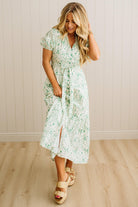Woman wearing a floral dress standing against a plain wall.