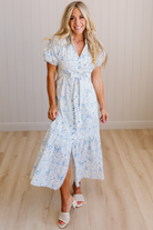 Woman wearing a white floral dress standing on a wooden floor with a light-colored wall background