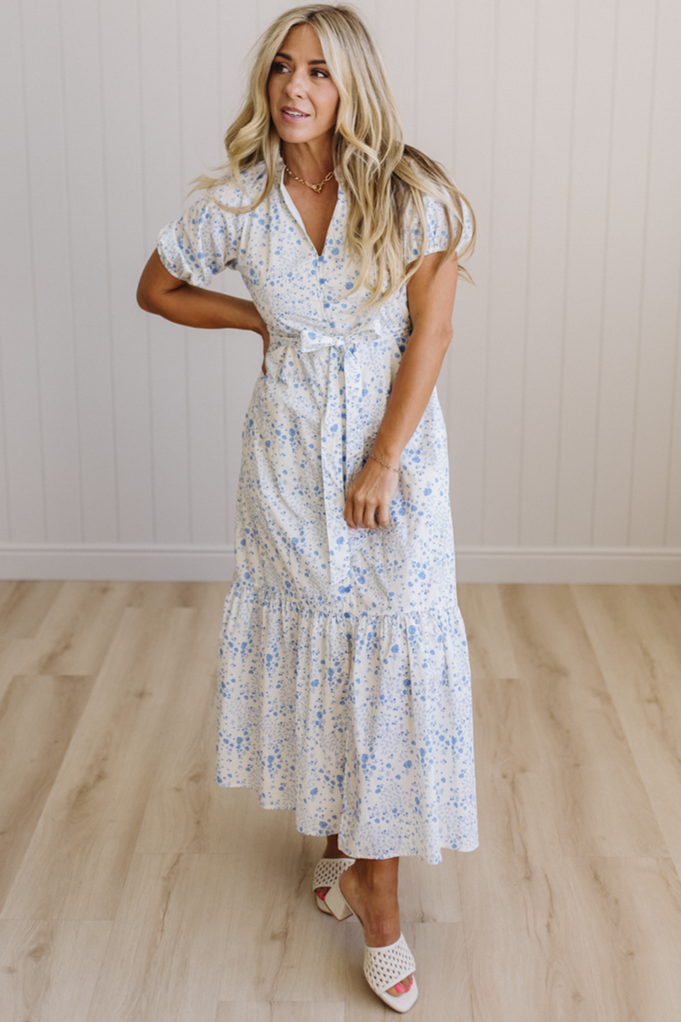 Woman wearing a white floral dress standing on a wooden floor with a light-colored wall background