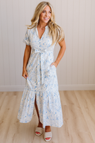 Woman wearing a floral dress standing on a wooden floor with a white paneled wall background