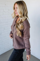 Woman wearing a brown sweater against a white brick wall.