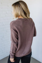 Person wearing a brown sweater against a white wall