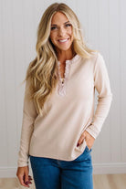 BLONDE WOMAN IN A BRIGHTLY LIT STUDIO WEARING DARK JEANS AND A SATIN RUCHED TRIM HALF BUTTON NECK, LONG SLEEVE, SOLID TOP IN IVORY