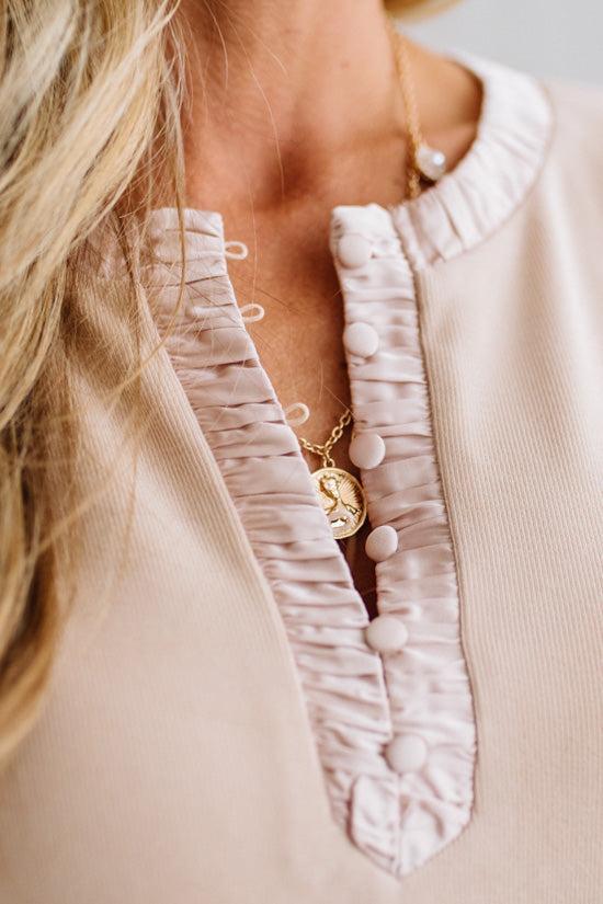 BLONDE WOMAN IN A BRIGHTLY LIT STUDIO WEARING DARK JEANS AND A SATIN RUCHED TRIM HALF BUTTON NECK, LONG SLEEVE, SOLID TOP IN IVORY