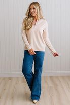BLONDE WOMAN IN A BRIGHTLY LIT STUDIO WEARING DARK JEANS AND A SATIN RUCHED TRIM HALF BUTTON NECK, LONG SLEEVE, SOLID TOP IN IVORY