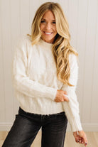 Woman wearing a white sweater and black pants against a light background