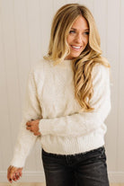 Woman wearing a white sweater and black pants against a neutral background