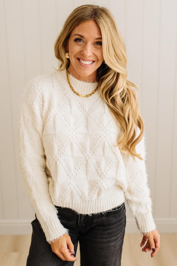 Woman wearing a white textured sweater and black pants against a neutral background