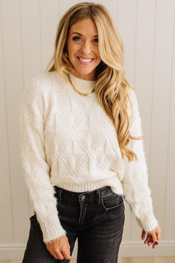 Woman wearing a white cable knit sweater and black jeans against a neutral background