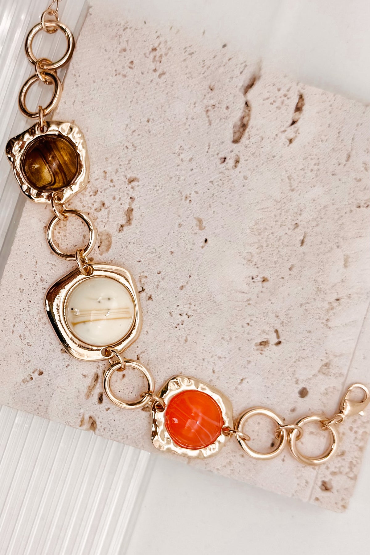 Interconnected Gold Ring Bracelet With Resin Marble Beads on a stone surface.