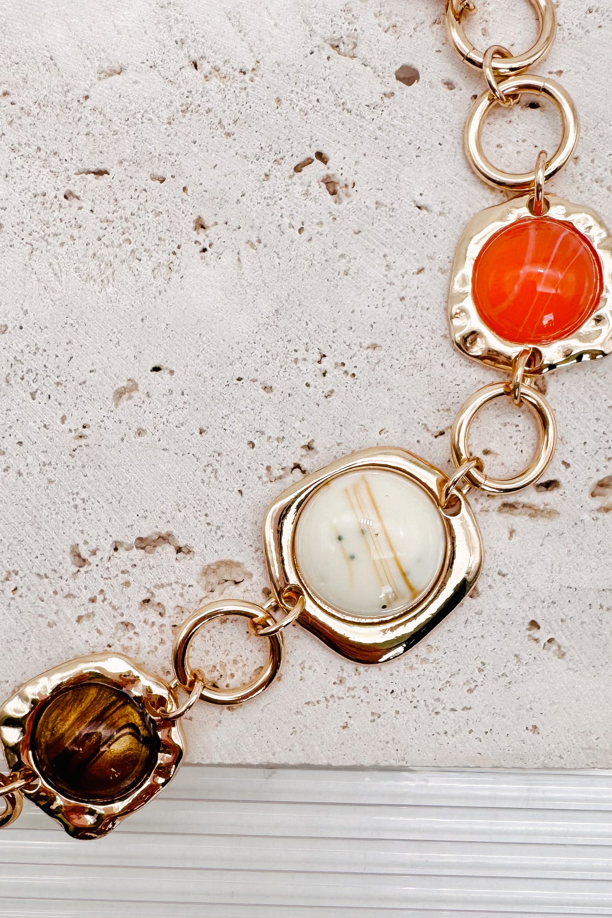 Interconnected Gold Ring Bracelet With Resin Marble Beads on a stone surface.