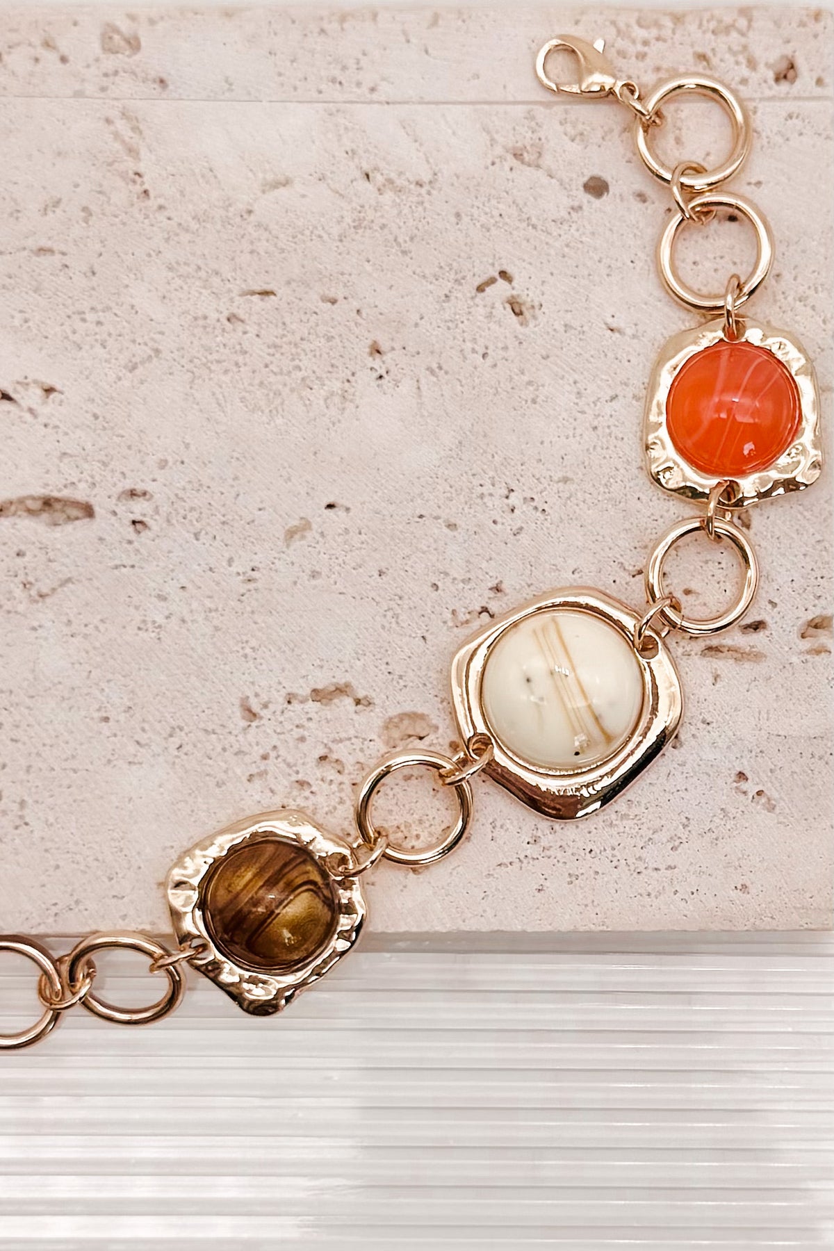 Interconnected Gold Ring Bracelet With Resin Marble Beads on a stone surface.