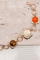 Interconnected Gold Ring Bracelet With Resin Marble Beads on a stone surface.