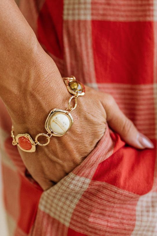 Interconnected Gold Ring Bracelet With Resin Marble Beads on a stone surface.