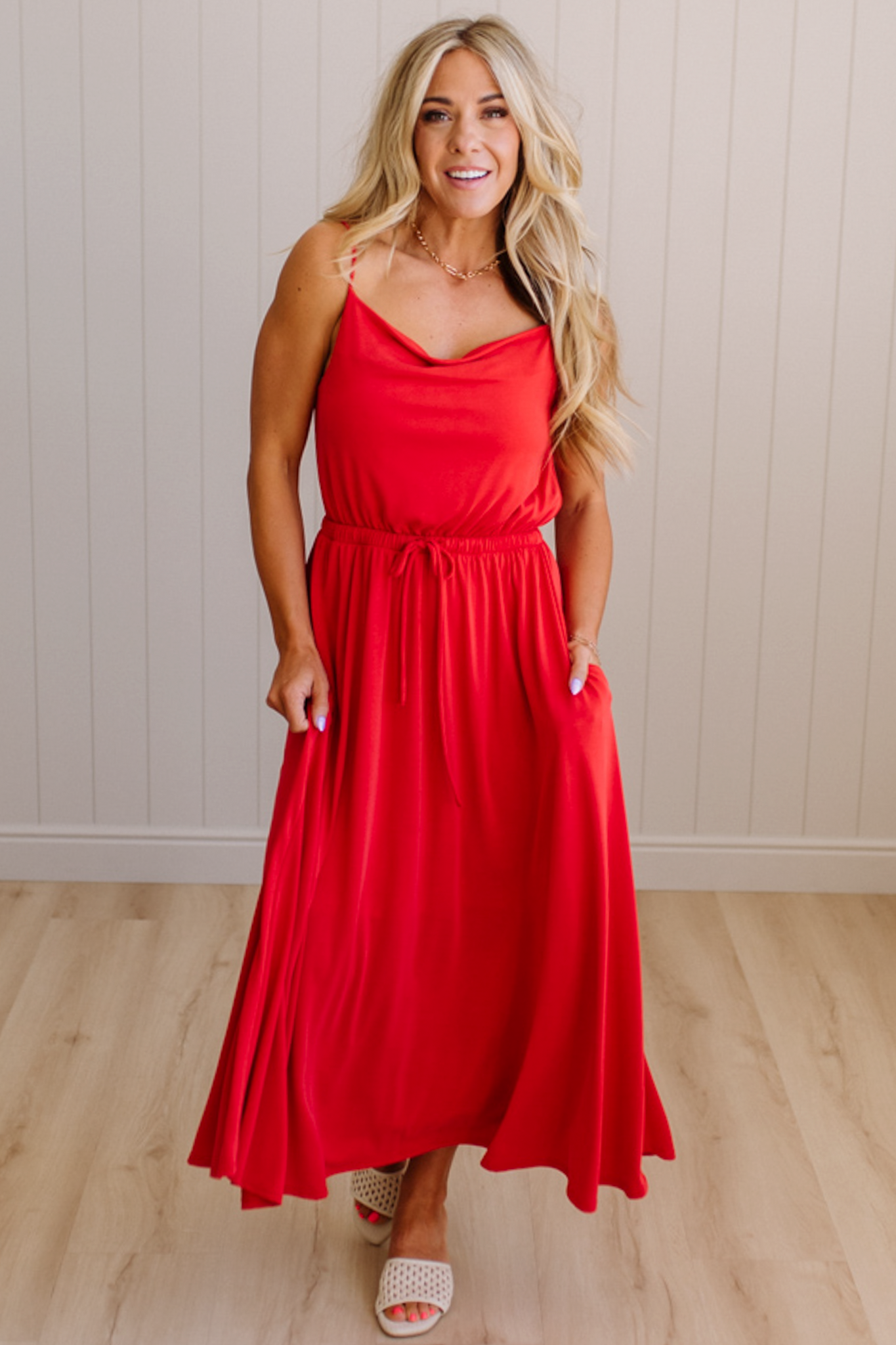 Woman wearing a red dress standing against a light wooden paneled wall.