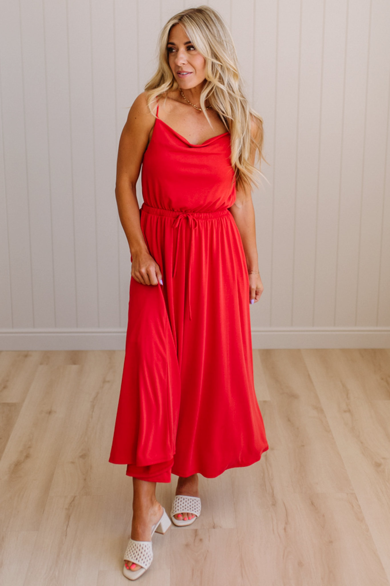 Woman wearing a red dress standing on a wooden floor with a white paneled wall in the background