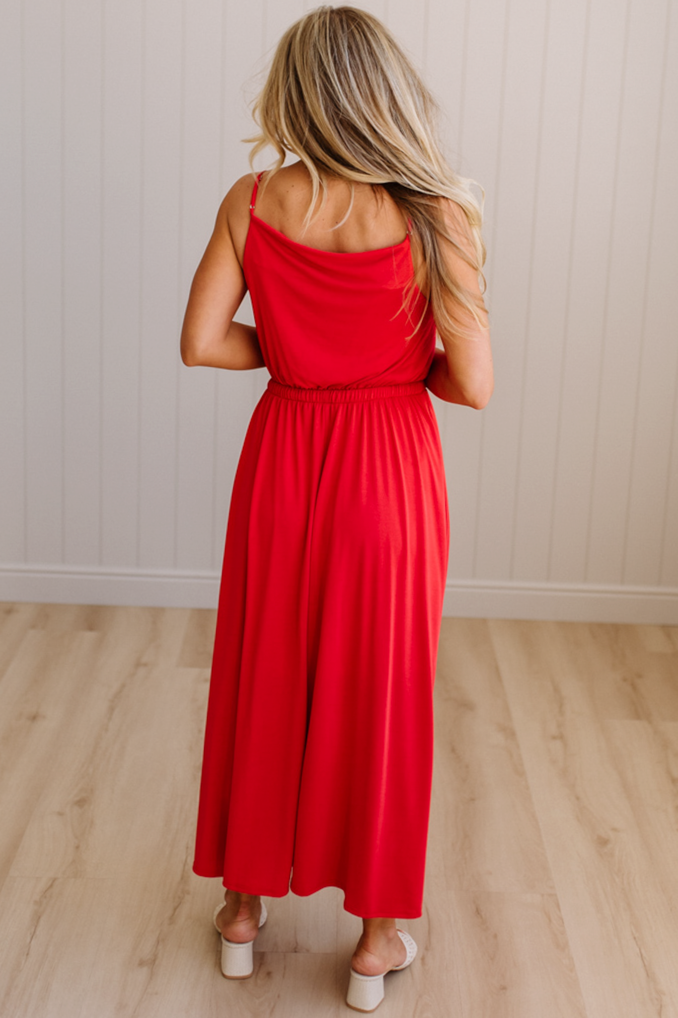 Woman wearing a red dress standing in a room with wooden flooring and a white wall.