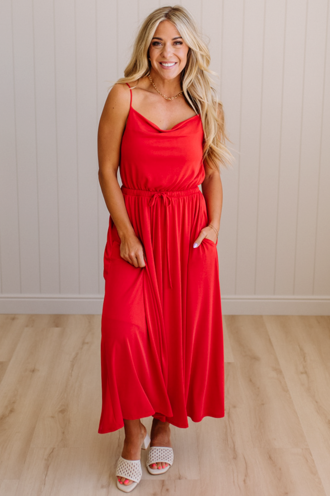 Woman wearing a red dress standing on a wooden floor with a white wall background