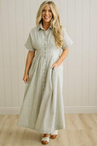 Woman wearing a checkered dress standing against a light wooden paneled wall.