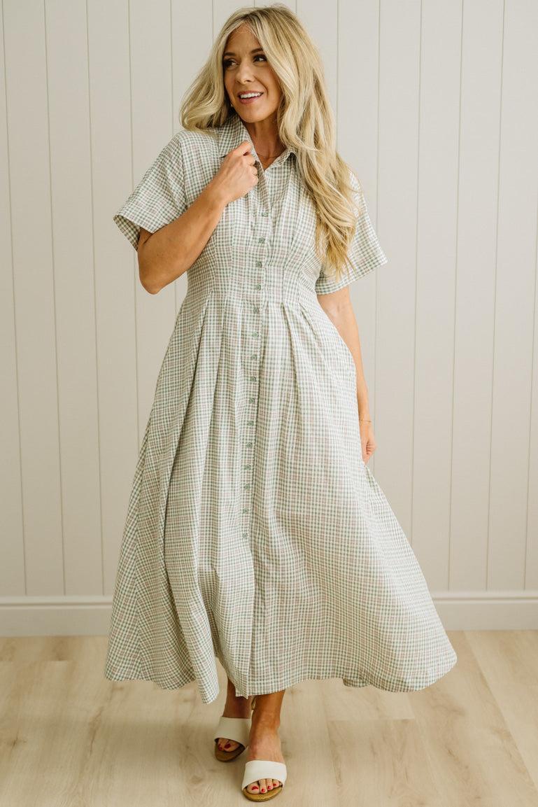 Woman wearing a checkered dress standing against a light wooden paneled wall.