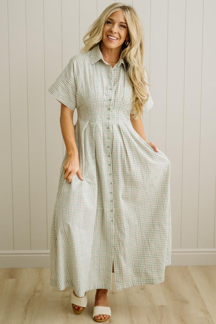 Woman wearing a checkered dress standing against a neutral wall.