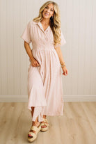 Woman wearing a pink and white striped dress standing against a light wooden paneled wall.