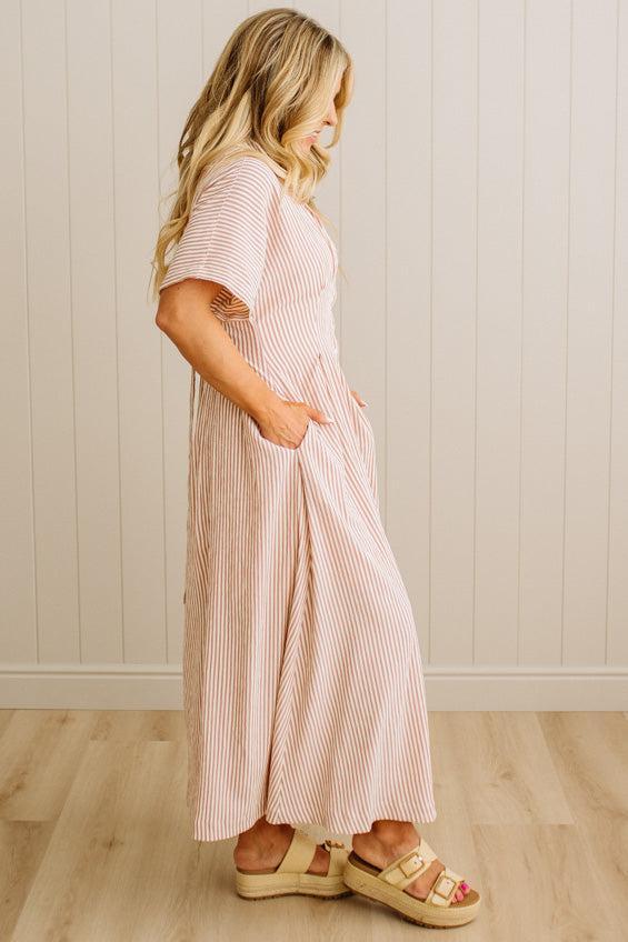 Woman wearing a pink and white striped dress standing against a white paneled wall.