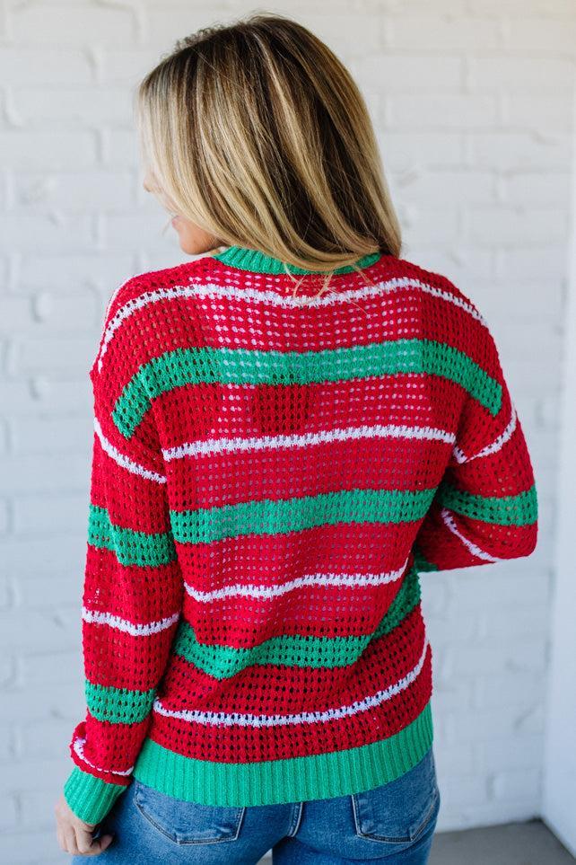 Person wearing a red, green, and white striped sweater against a white brick wall.