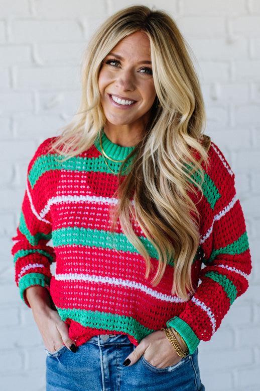 Woman wearing a red, green, and white striped sweater against a white brick wall.