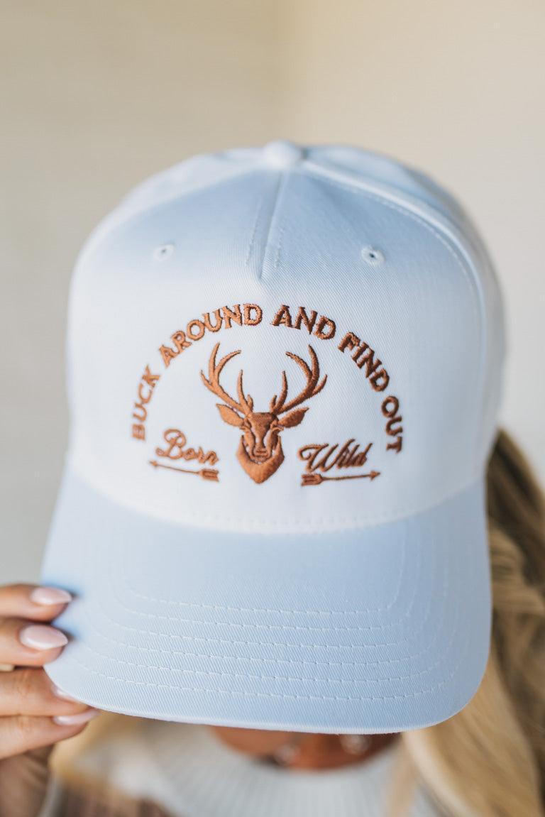 White cap with embroidered text and deer design held by a person.