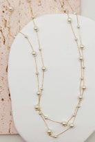 Two-layered pearl necklace on a white surface with a textured pink background