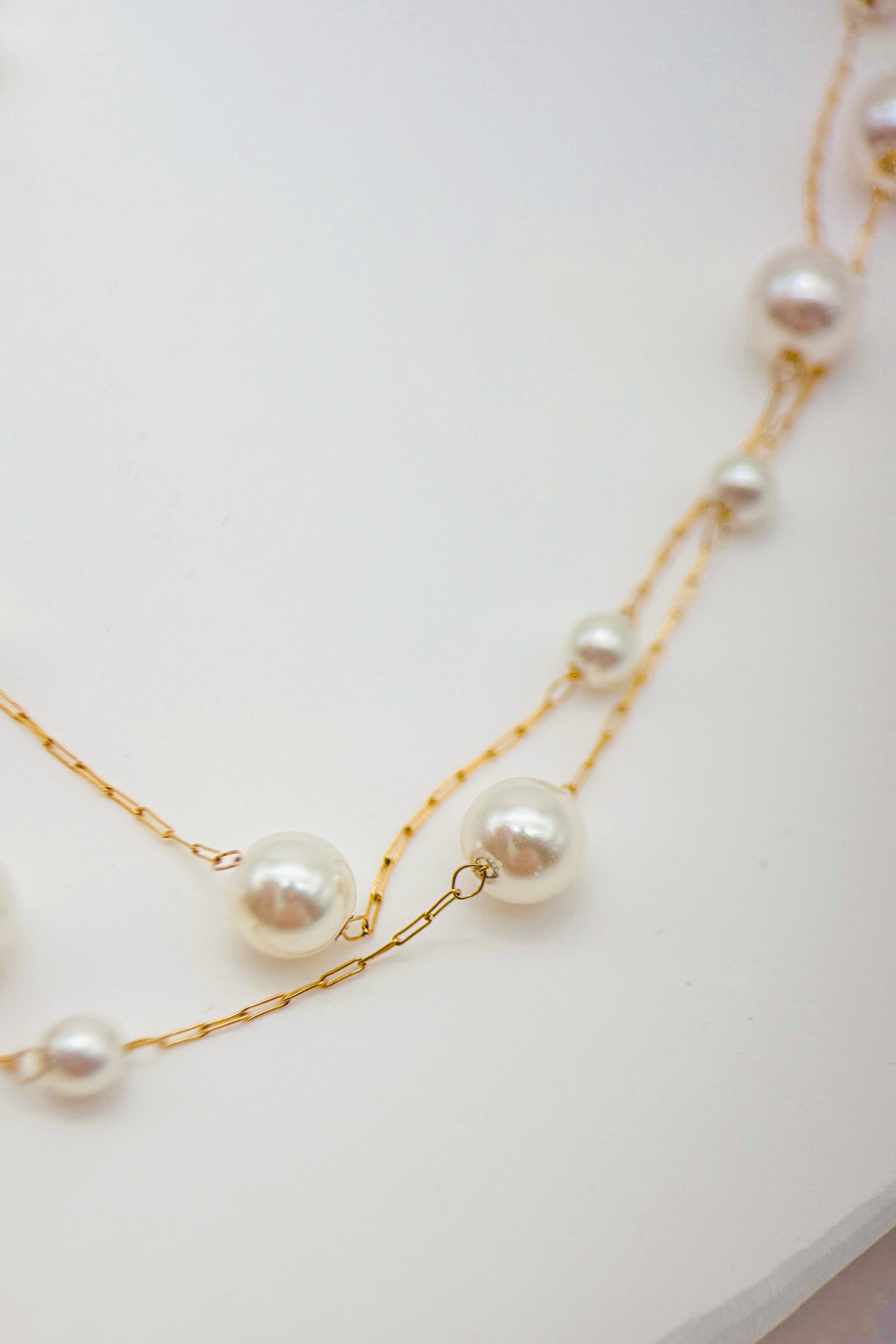 Pearl necklace with gold chain on a white surface