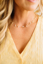 Pearl necklace worn by a person with blonde hair and a yellow top.