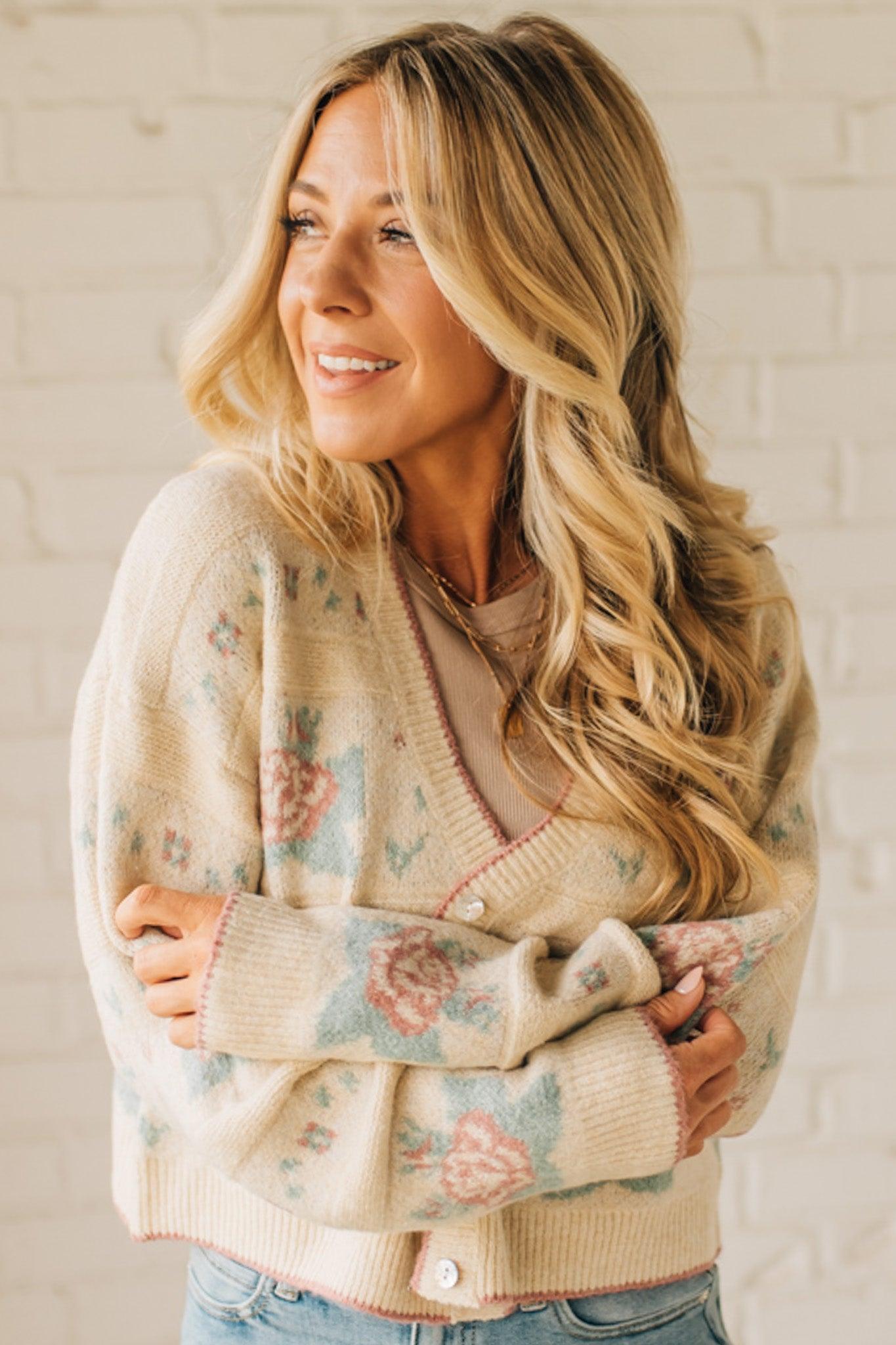 Woman wearing a floral cardigan against a white brick wall