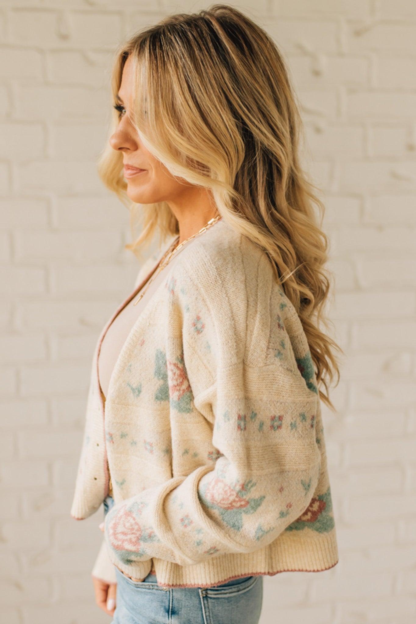 Woman wearing a floral cardigan against a white brick wall