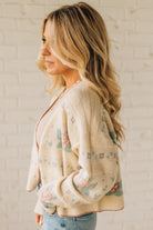 Woman wearing a floral cardigan against a white brick wall