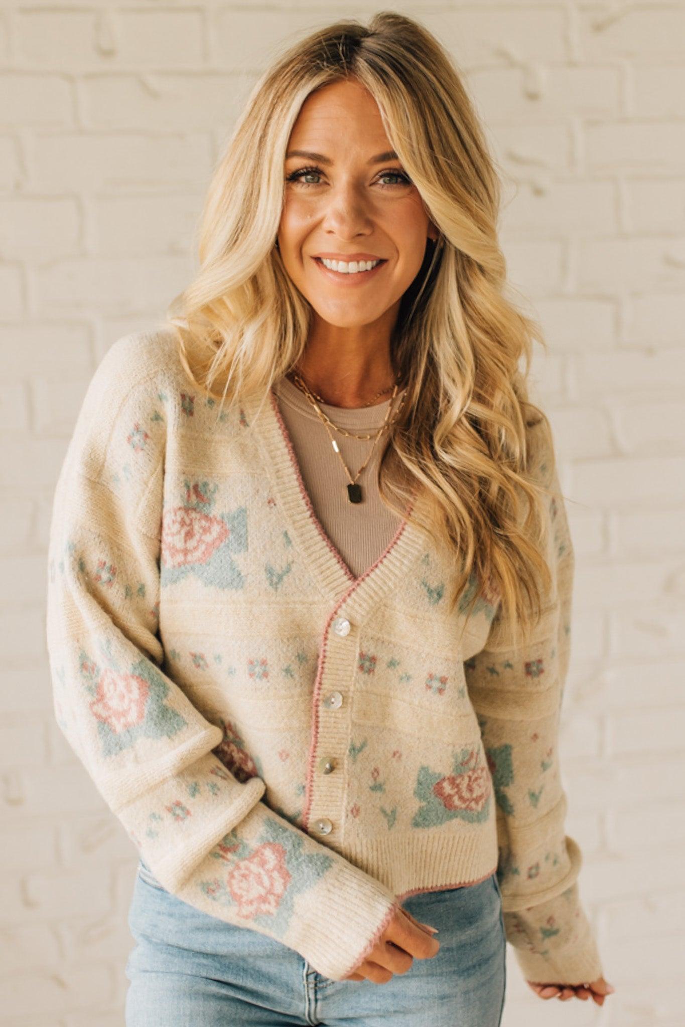 Woman wearing a floral patterned cardigan against a white brick wall