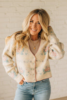 Woman wearing a floral cardigan with a white brick wall background