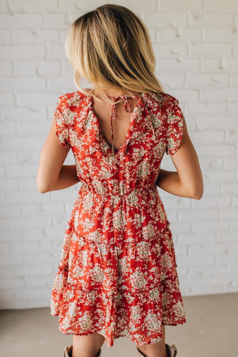 Woman wearing a red floral dress against a white brick wall.